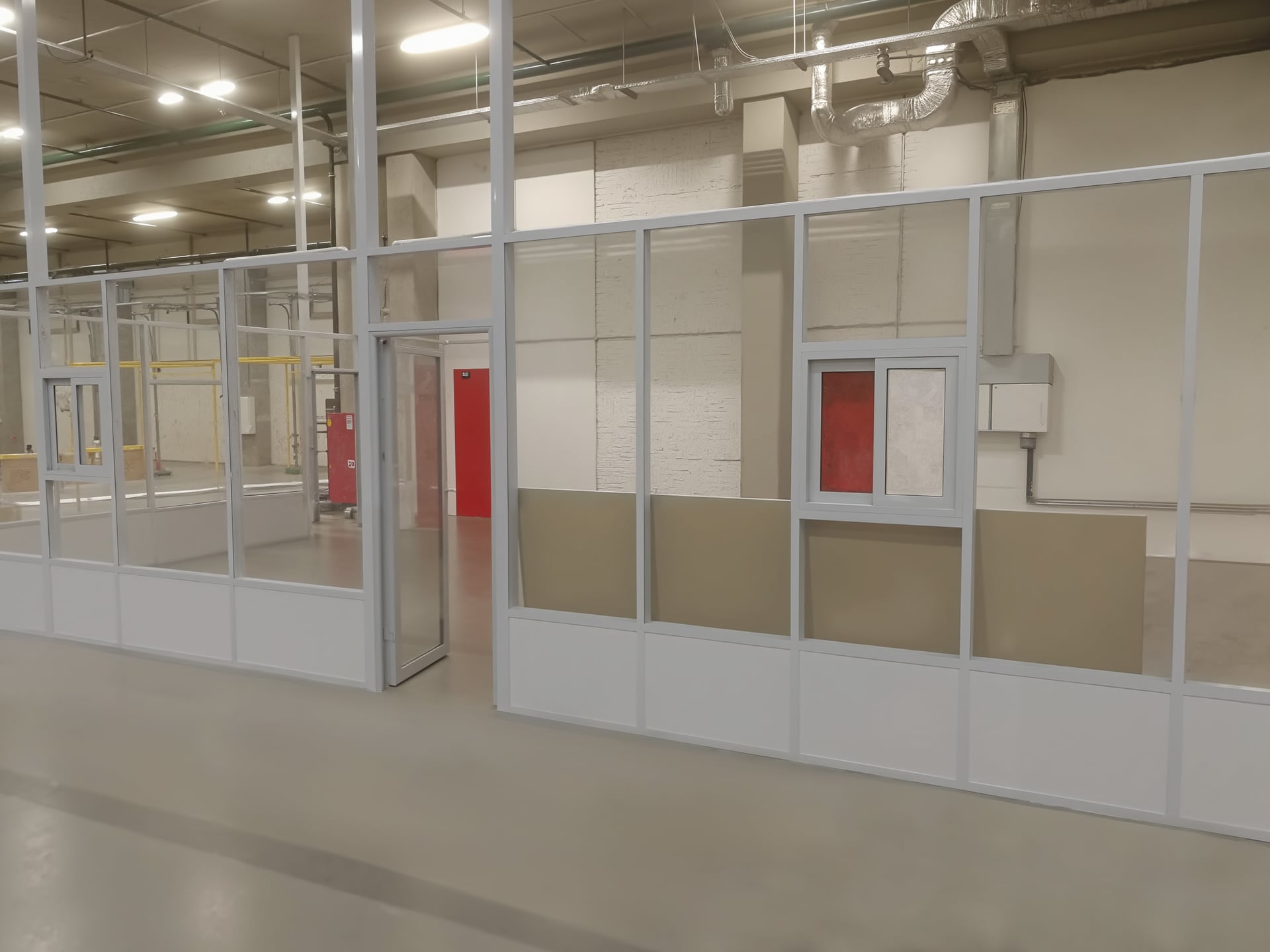 Серые алюминиевые перегородки из стекла и глухих панелей, с окошками, в производственном помещении. Серые алюминиевые перегородки в производственном помещении