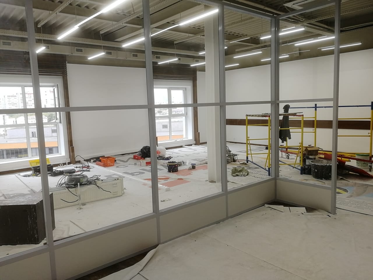 Каркас до заказа стекла Монтаж перегородок из стекла, каркас без заполнения: проёмы пока пустые, пол укрыт, у окна леса