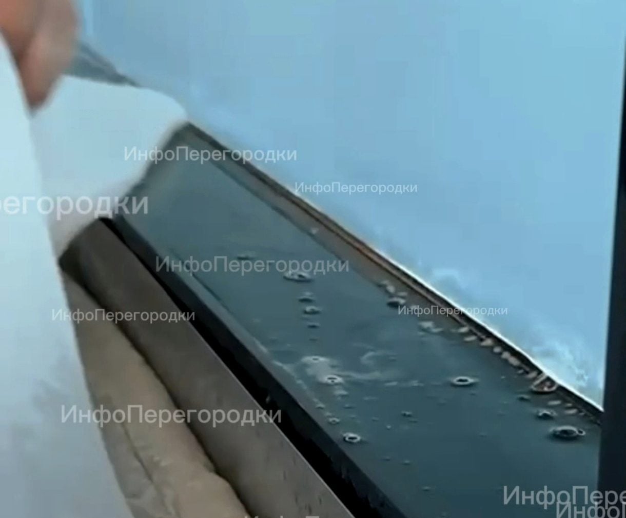 Крупно: рука ведёт инструментом по краю плёнки, на стекле капли воды Тонировка плёнкой: край полотна прикатывают к стеклу у самого профиля