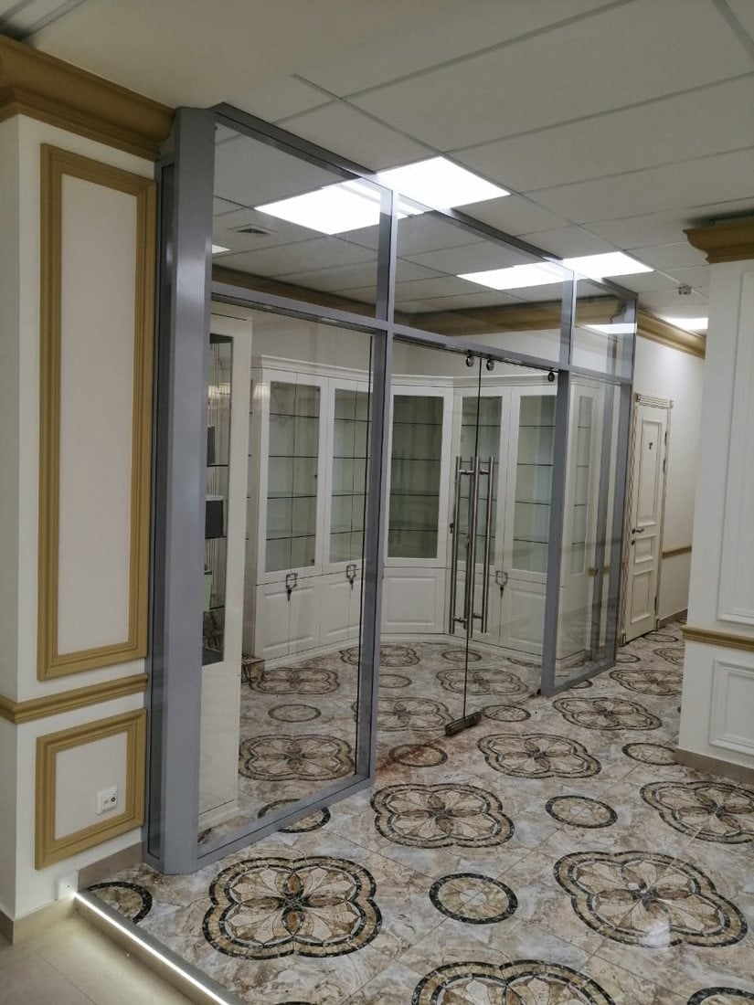 Стекло в сером алюминиевом профиле в медцентре Угол перегородки для медцентра: широкие стеклянные секции в сером профиле до потолка и дверь из стекла