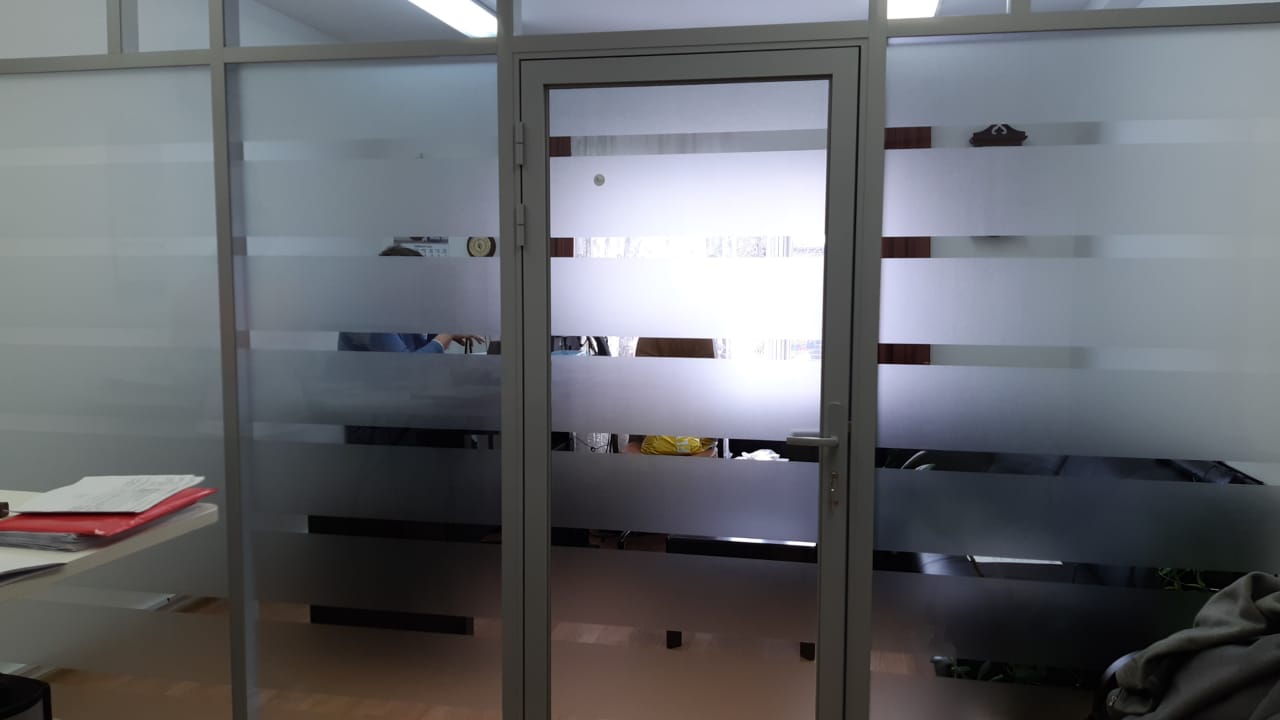 Стеклянная перегородка с матовой полосатой плёнкой и дверью в офисе Офисная перегородка с матовыми горизонтальными полосами и дверью — приватность кабинета без потери света